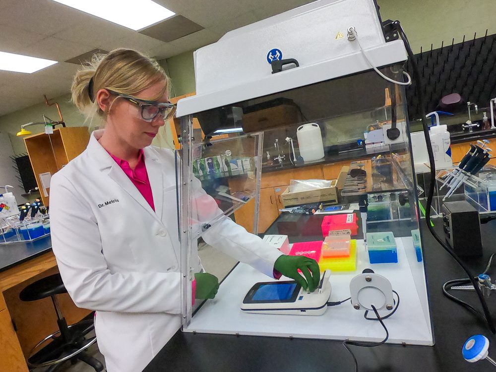 A woman wearing a white coat works in a Clemson University laboratory.