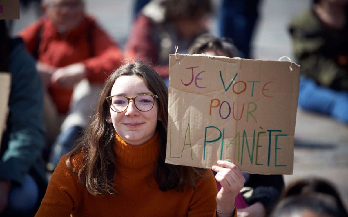A young woman is holding up a cardboard sign with reading "I vote for the plant"