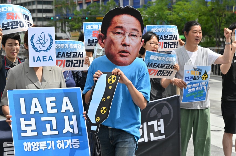 South Korean protesters hold a rally against Fukushima's water release plan.  One wears a mask of Japanese Prime Minister Fumio Kishida.  Others have signs in Korean that read IAEA 