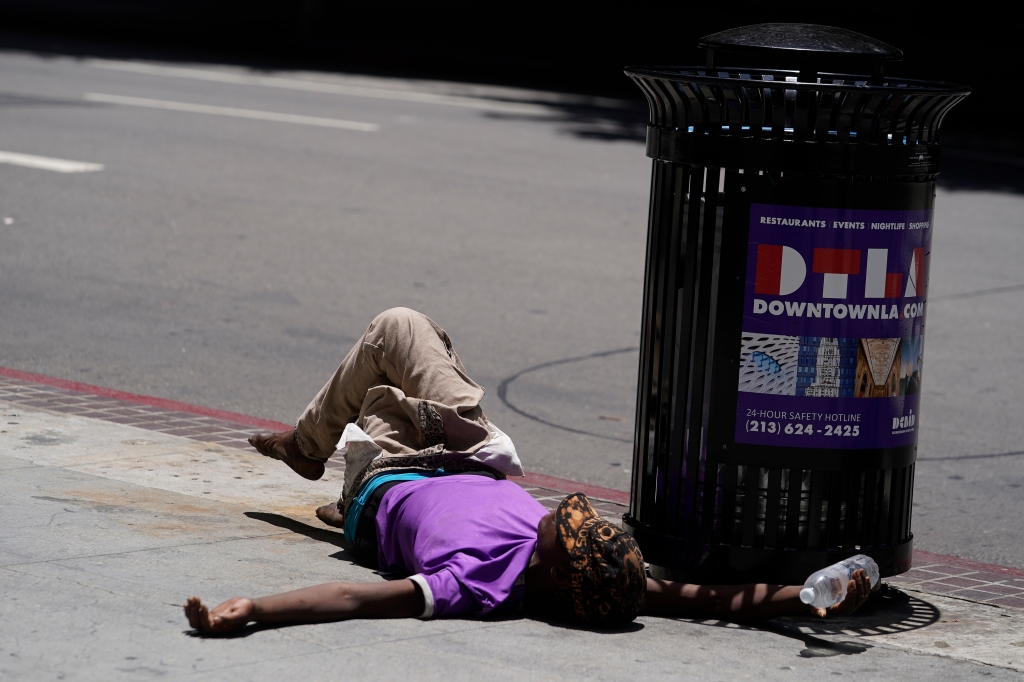 A homeless man lies on the sidewalk while holding a bottle of water, Sunday, July 2, 2023, in downtown Los Angeles. 