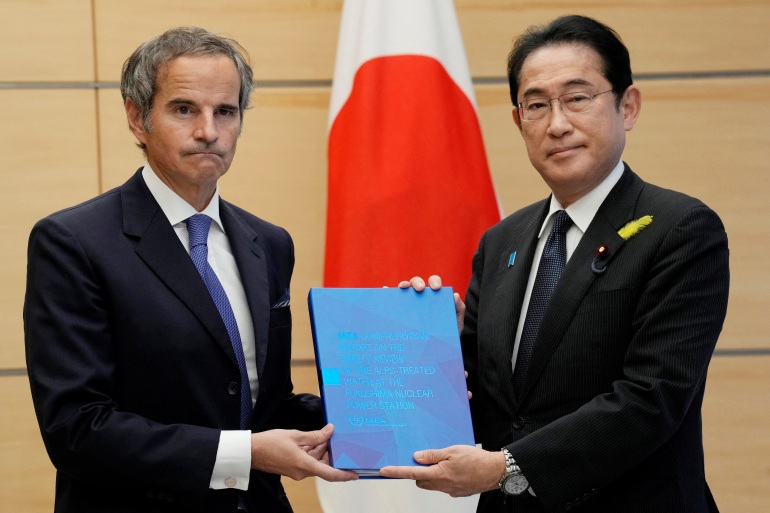 IAEA chief Rafael Grossi delivers Fukushima water release plan report to Japanese Prime Minister Fumio Kishida.  The report is blue.  There is a Japanese flag behind them.