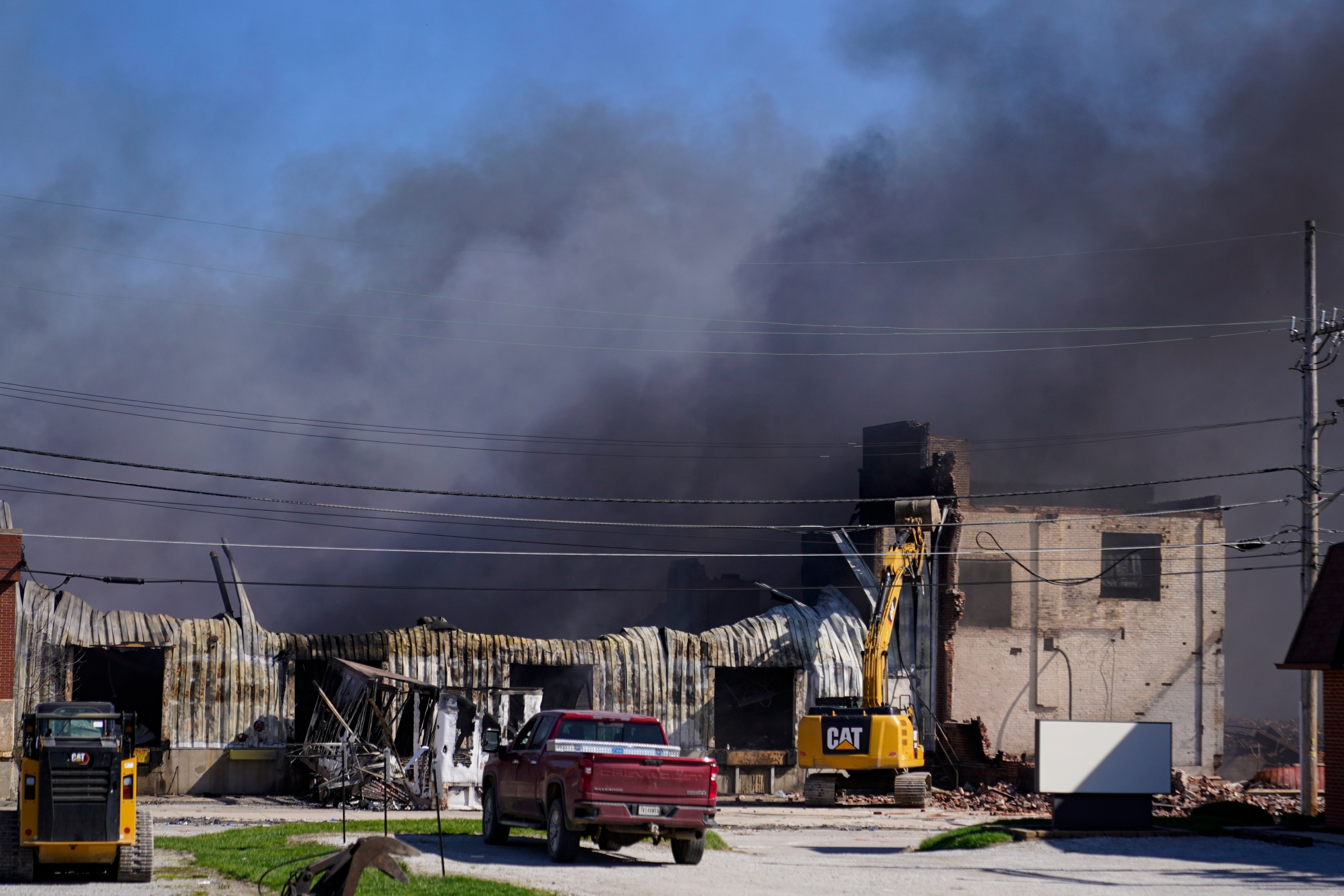 Workers tear down a section of the site of an industrial fire in the area as smoke billows from the site in Richmond, Indiana on Wednesday, April 12, 2023. Authorities have urged people to evacuate if they live near the blaze.  The former factory site was used to store plastics and other materials for recycling or resale.  (AP Photo/Michael Conroy)
