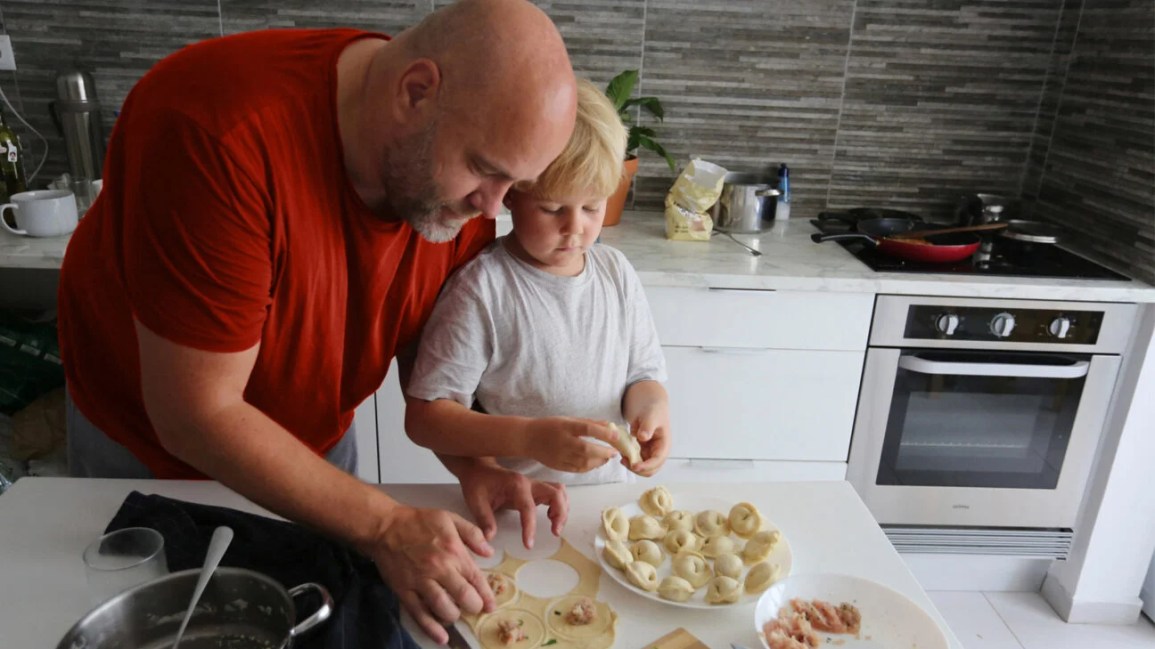 A father helps his son cook a dish.